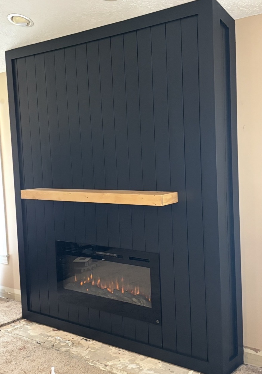 Custom black media wall with electric fireplace and natural wood mantel built by K.C. Elite